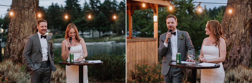 A man in a gray suit and a woman in a white dress stand at a round table outdoors, speaking into microphones during an evening event.